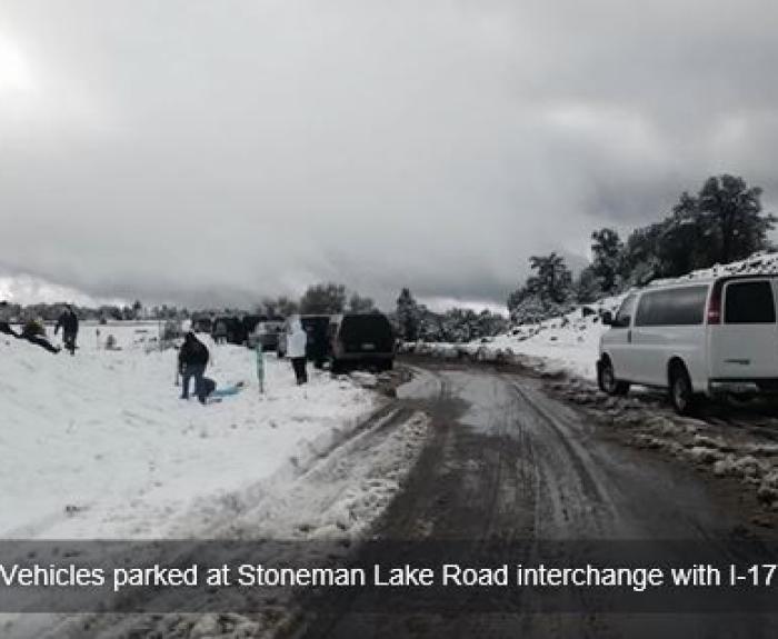 Several vehicles are parked at the Stoneman Lake Road interchange with I-17 and people are standing around in the snow at the roadside.