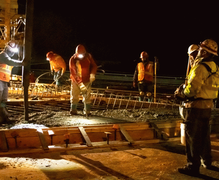 Workers pouring concrete bridge deck at night
