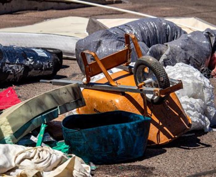 Assorted discarded items, including an overturned orange wheelbarrow, fabric, and plastic containers, scattered on a paved surface.