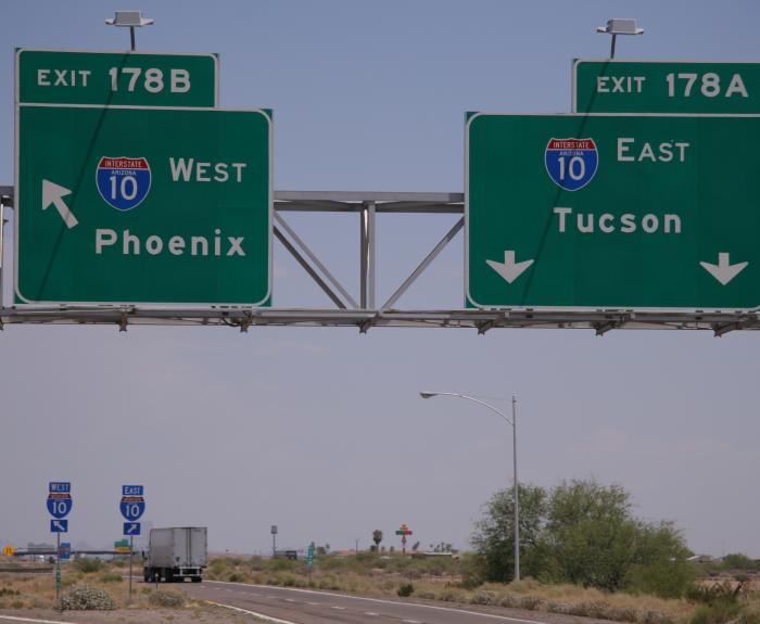 Overhead highway signs show directions for I-10 West to Phoenix (Exit 178B) and I-10 East to Tucson (Exit 178A) above a road with a truck driving.