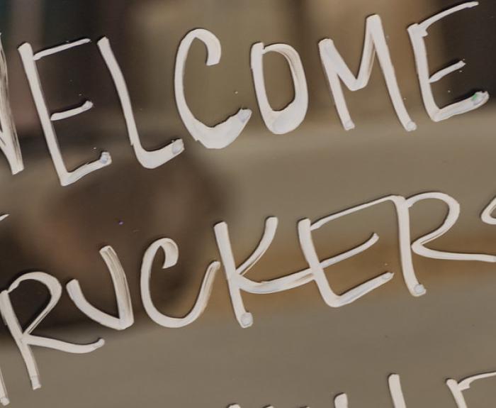 White handwritten text on a window or glass says WELCOME TRUCKERS with a blurred indoor background visible behind the writing.