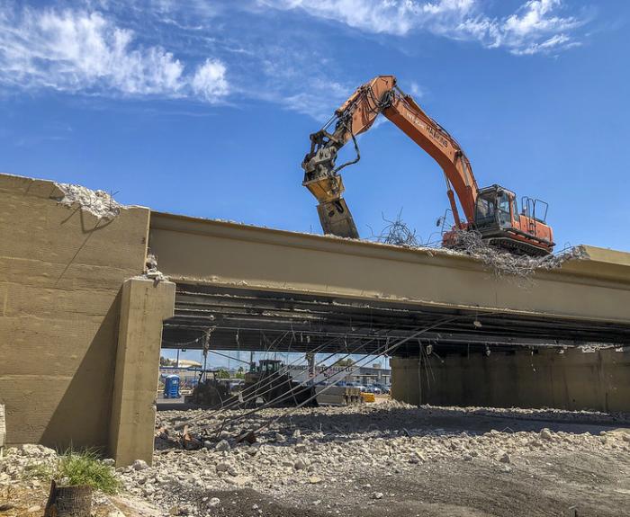 An excavator demolishes the top of a concrete bridge.
