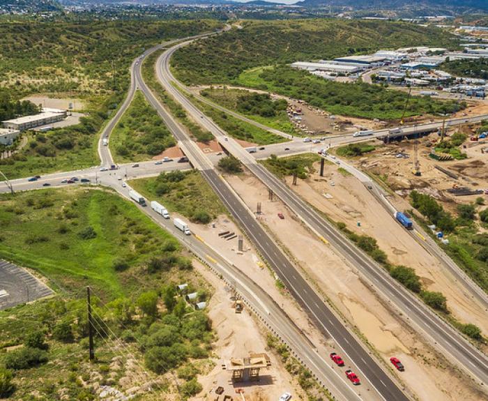 Aerial view of a highway intersection with surrounding greenery and some buildings under a partly cloudy sky.