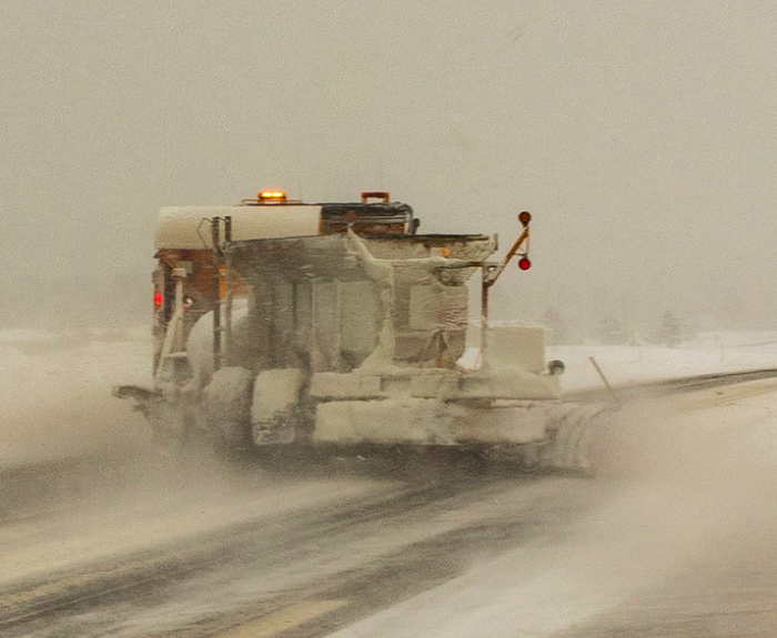 A snowplow clears a snow-covered road in low visibility during a winter storm.