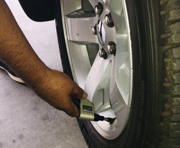 A person checks the air pressure of a car tire using a digital tire pressure gauge, with the gauge pressed against the tire’s valve stem.