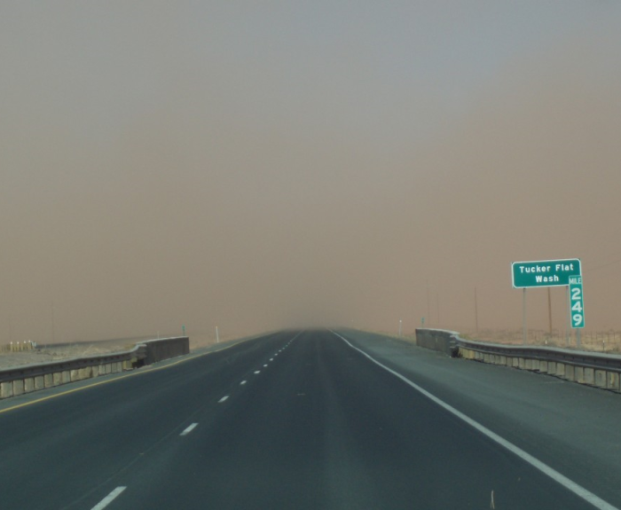A highway stretches forward under a hazy sky with reduced visibility. A green road sign reads Tucker Flat Wash and 242.