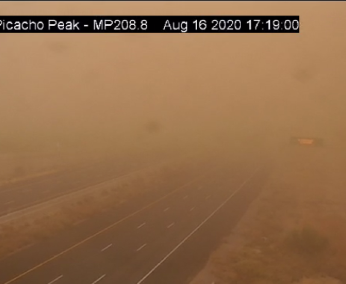 A highway near Picacho Peak is barely visible due to thick dust from a sandstorm, with very low visibility and a faint traffic sign in the background.