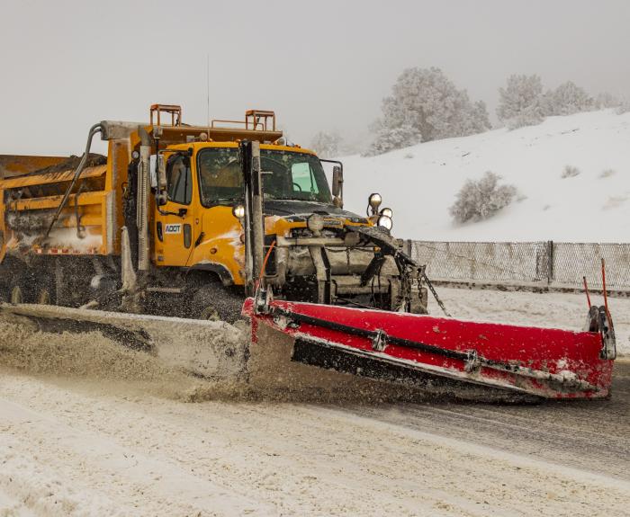 A snowplow clearing ice and snow off the highway. 