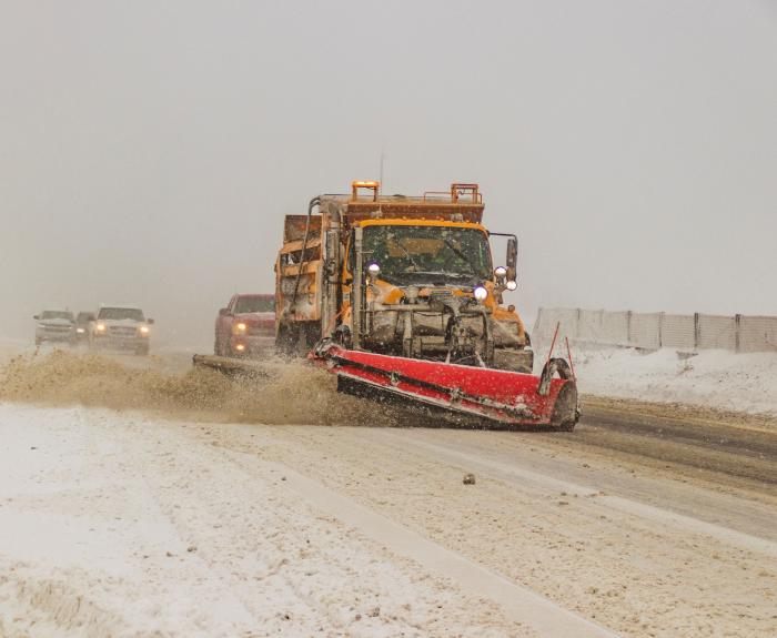 A snowplow clearing ice and snow off the highway. 