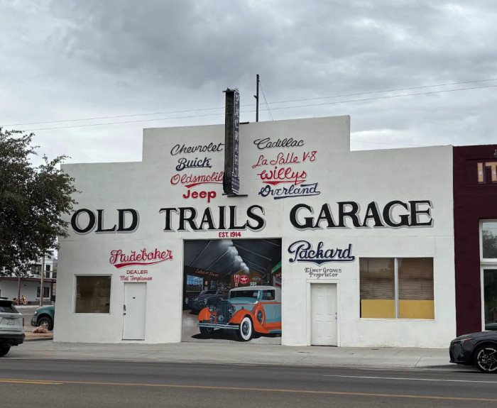 A full color image shows the Old Trails Garage as it is now. The building is white with a mural on the front that appears to look into the garage, with painted vehicles.