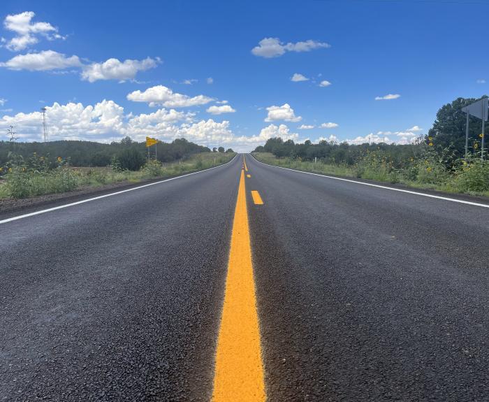 image of a roadway with fresh asphalt and yellow lane striping.