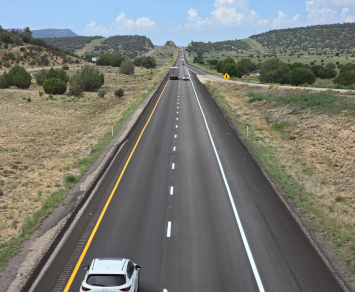 Image of freshly paved road lying straight through green grass on either side. 