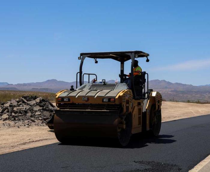 Man on steam roller drives over fresh black asphalt.